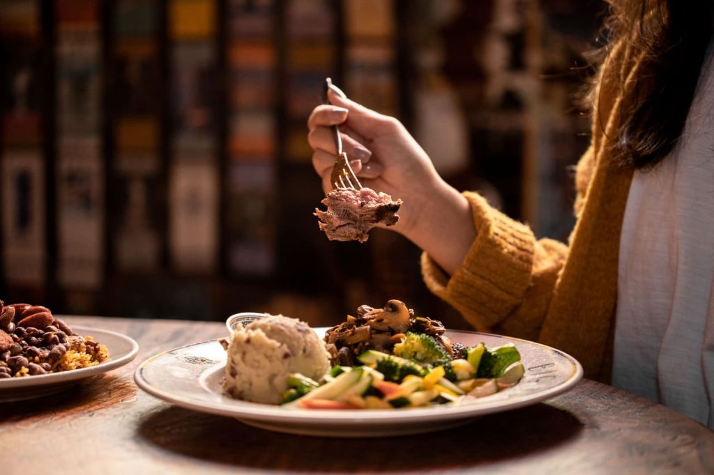 Jazz - A Louisiana Kitchen A person holding a forkful of food above a plate with mashed potatoes, vegetables, and meat in a cozy dining setting. Kansas City, Columbia
